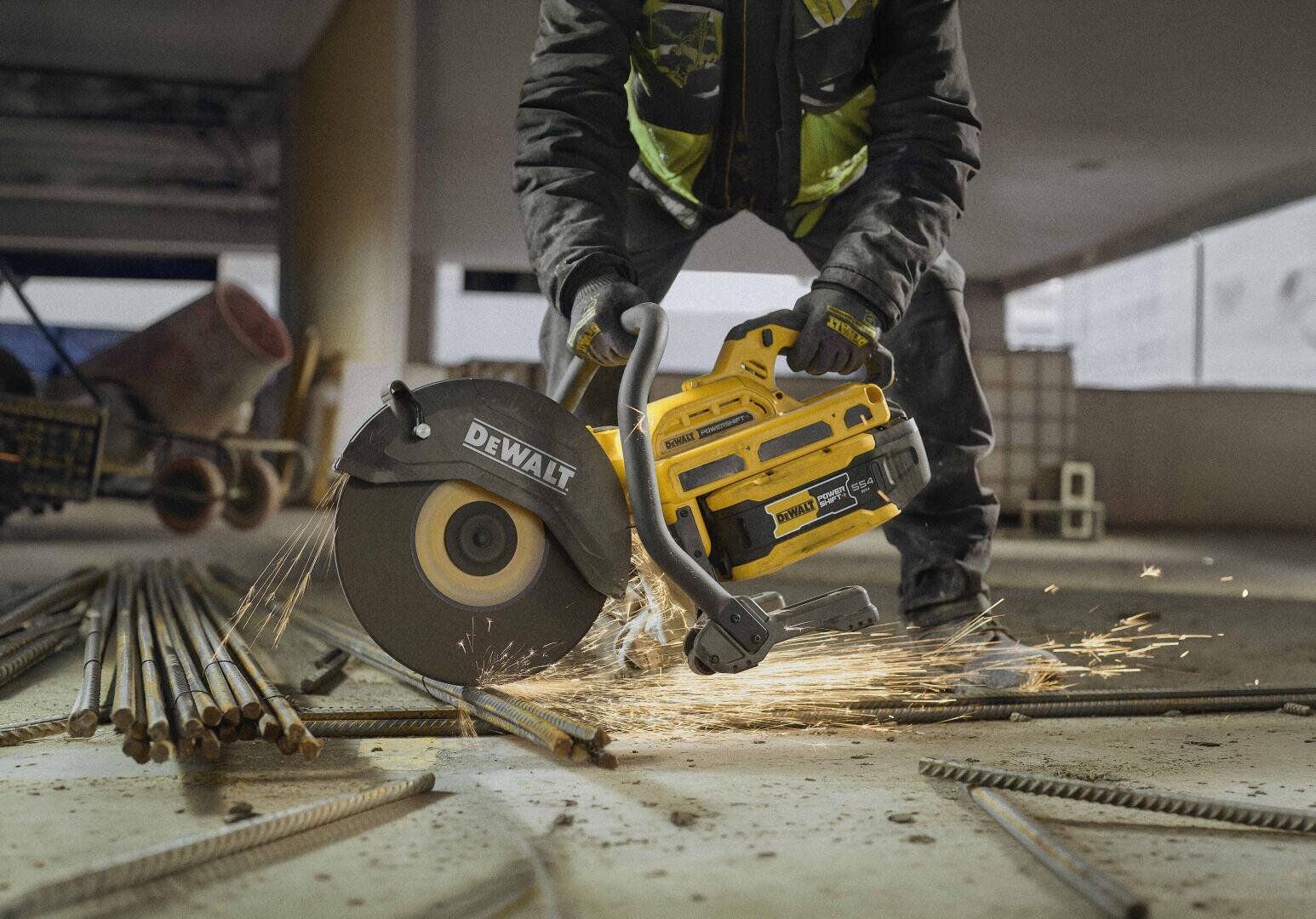 Ein Arbeiter schneidet mit einer gelben Akku-Trennschleifmaschine der Marke DeWalt durch Metallbewehrungsstäbe, wobei eine Funkenfontäne entsteht.