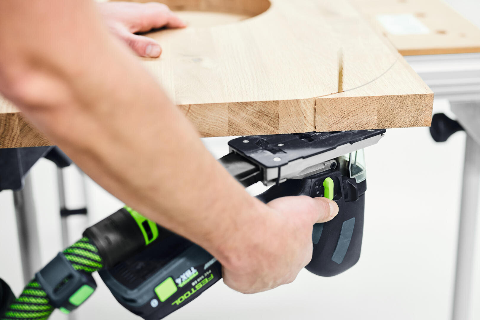 Eine Person schneidet mit einer Handstichsäge eine geschwungene Linie in ein Holzbrett.