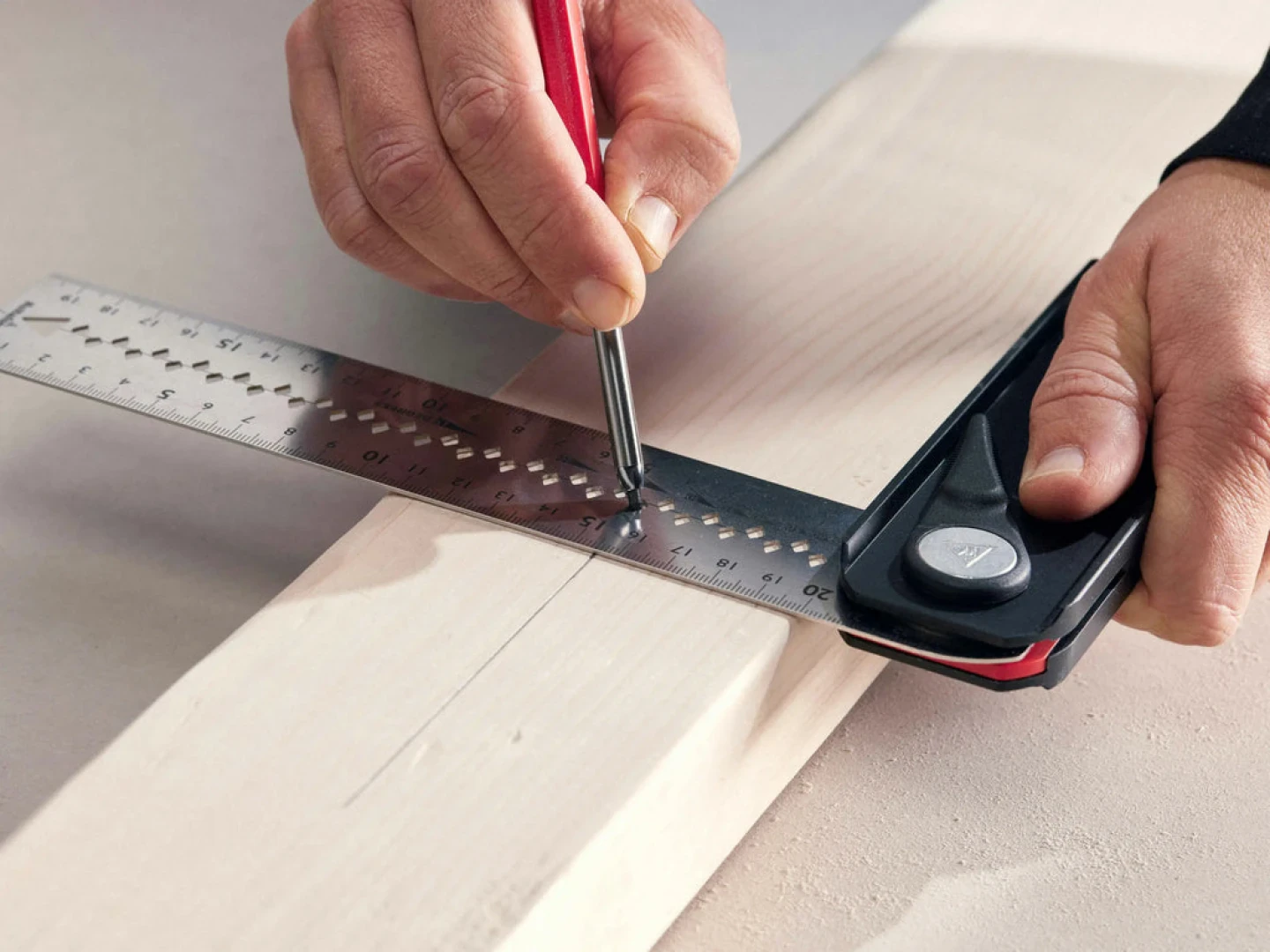 Eine Person verwendet ein Kombinationswinkel aus Metall und einen Bleistift, um eine gerade Linie auf einem Stück hellem Holz zu markieren und es so zum Schneiden oder Messen vorzubereiten.