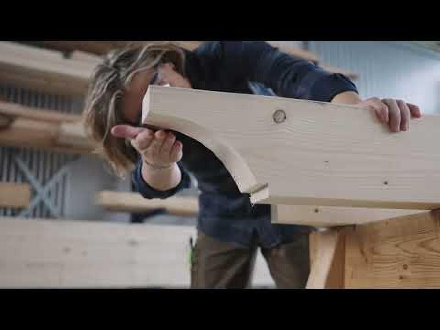 Un menuisier examine le bord incurvé d'une grosse poutre en bois dans un atelier.
