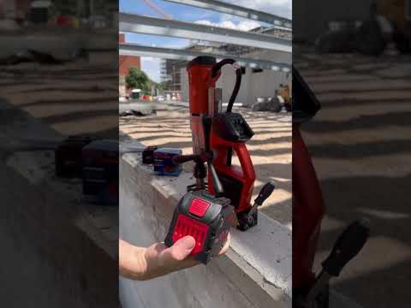 Eine Person, die auf einer Betonbaustelle eine rote, kabellose Magnetbohrmaschine in der Hand hält.