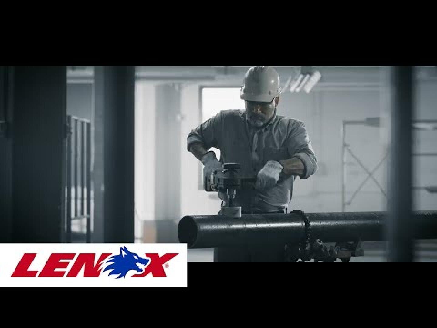 Ein Arbeiter in Schutzkleidung schneidet mit einem Elektrowerkzeug in einem Innenraum ein Metallrohr durch. In der unteren linken Ecke ist das Lenox-Logo mit einem blauen Wolf zu sehen.