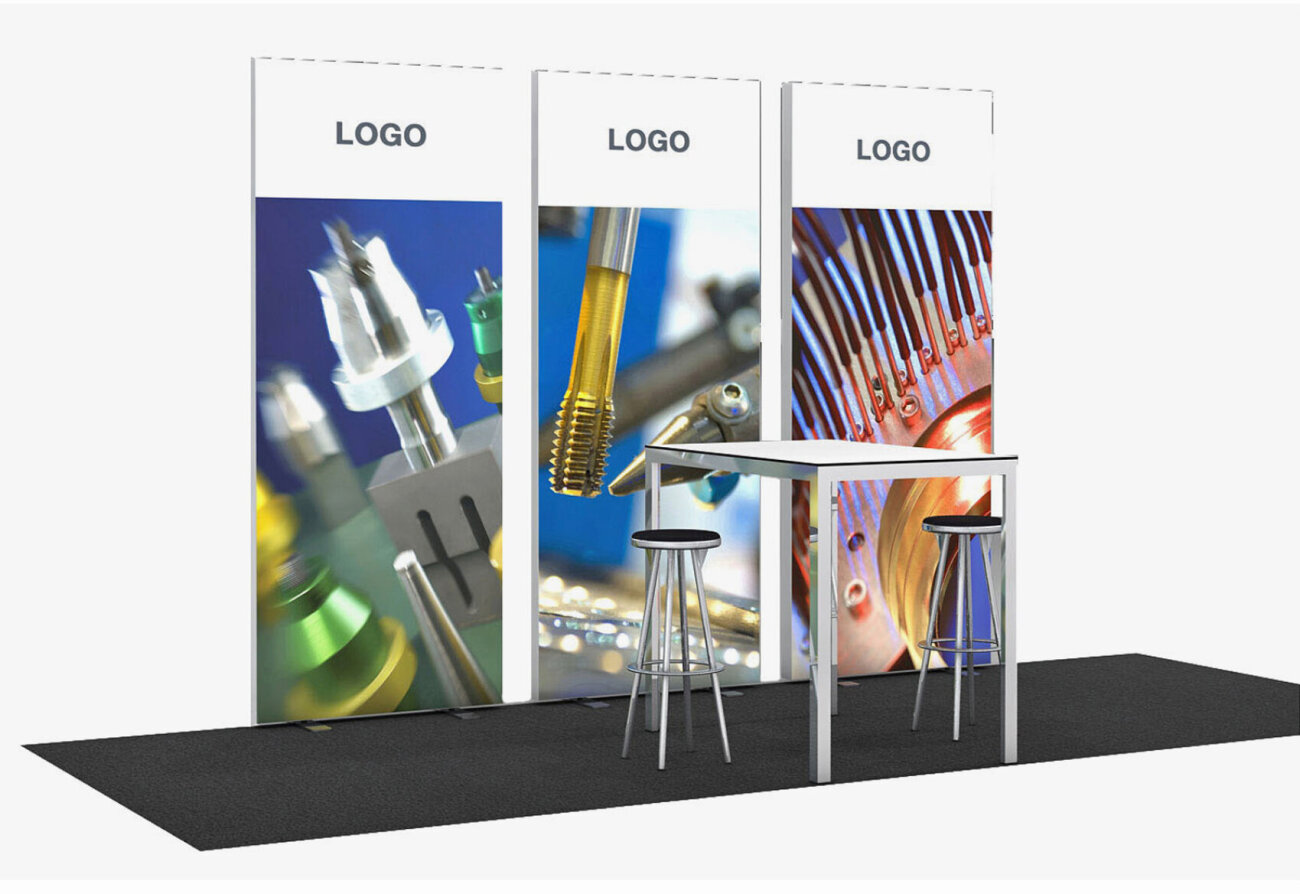 Ein Messestand mit drei weissen Rückwänden, die jeweils mit dem Platzhalter 'LOGO' beschriftet sind. Die Wände sind mit grossformatigen technischen Bildern bedruckt. Vor den Wänden steht ein hoher, schlichter Tisch mit zwei Metallhockern. Der Stand befindet sich auf einer schwarzen Teppichfläche.